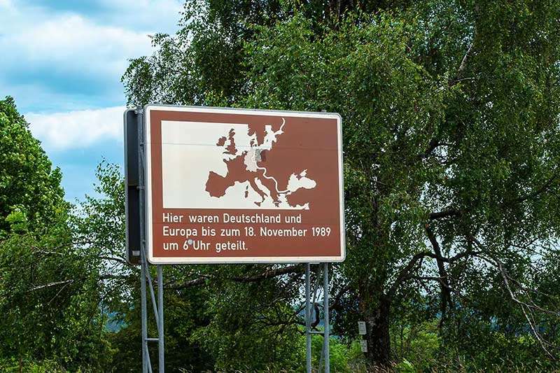 Braunes Hinweisschild am ehemaligen Grenzverlauf mit einer Karte Europas und dem Hinweis, dass Deutschland und Europa hier bis zum 18. November 1989 geteilt waren.